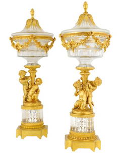 A PAIR OF BACCARAT STYLE CRYSTAL AND BRONZE DORE CO: A PAIR OF BACCARAT STYLE CRYSTAL AND BRONZE DORE COVERED URNS Each bronze dore pineapple finial with acanthus leaves draping over the crystal cover and seats into a bronze dore cast swagged collar sup