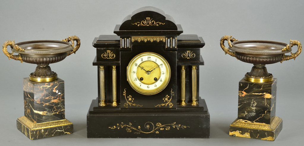 A VINTAGE "W. BISHOP & SON" MANTEL CLOCK WITH A PA: A VINTAGE ""W. BISHOP & SON"" MANTEL CLOCK WITH A PAIR OF URNS 20th Century A large black stone carved mantel clock having an arched pediment, gilt foliate, four flanking columns, raised on a plinth b