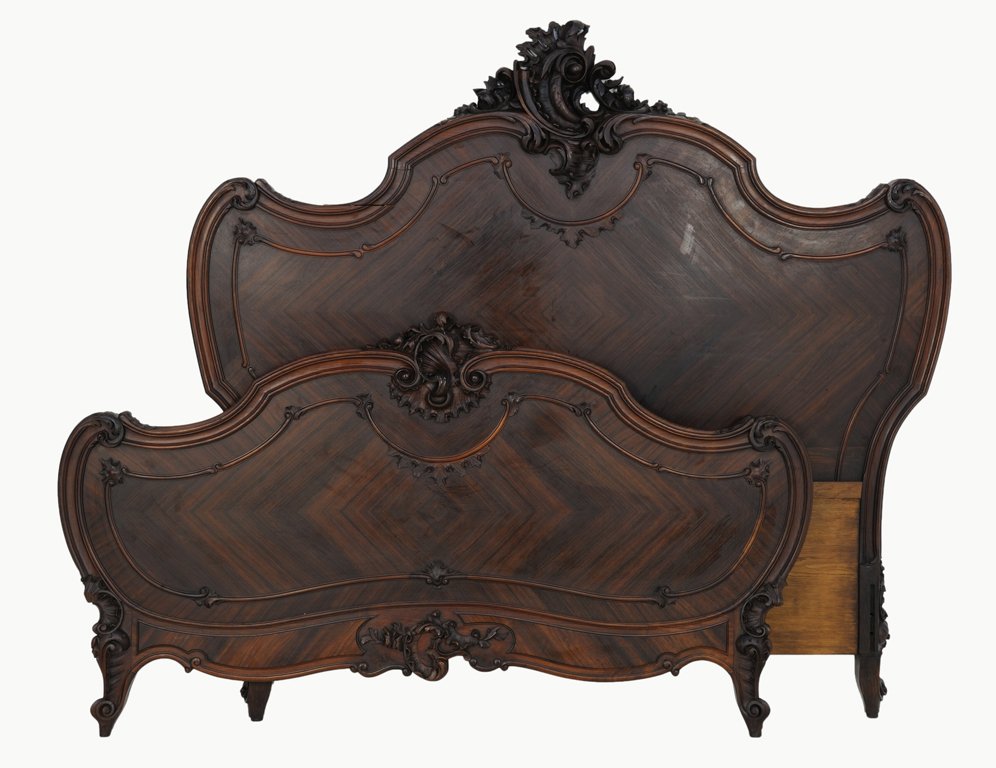 A LOUIS XV STYLE ROSEWOOD BED: A LOUIS XV STYLE ROSEWOOD BED Early 20th Century An elaborately carved rosewood ""scrollform"" acanthus leaf above a humpback crest rail is flanked by c-scrolls at the corners; raised on scrollform fe