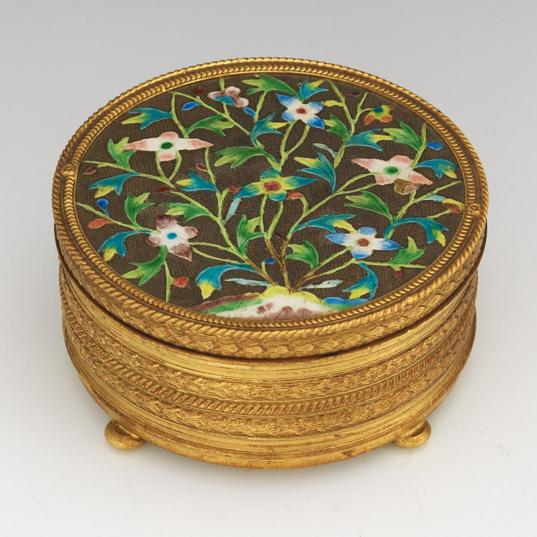 Apollo Studios Gilt Bronze Powder Box: 2-3/8" x 4-3/4" Round bronze box with Chinese Export style silver enameled floral lid inset, on four bun feet and signed to the underside. Clear glass insert. View and Bid on Asp