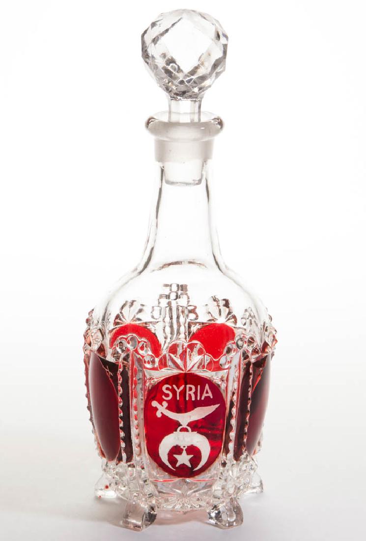 PENTAGON VARIANT - RUBY-STAINED WINE DECANTER: PENTAGON VARIANT - RUBY-STAINED WINE DECANTER, colorless, engraved Masonic decoration, pressed-facet stopper. Maker unidentified. Circa 1890. 10" HOA. Decanter undamaged, stopper with a chip to the ex