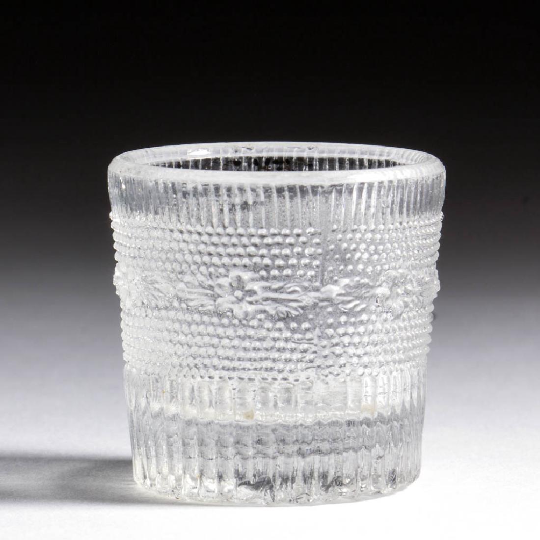 PRESSED LACY TOY TUMBLER: PRESSED LACY TOY TUMBLER, colorless, short cylindrical form with a medial band of blossoms and leaves separating bands of fine ribs, rayed base with central dot. Probably Midwestern. 1835-1850. 1 1/8"