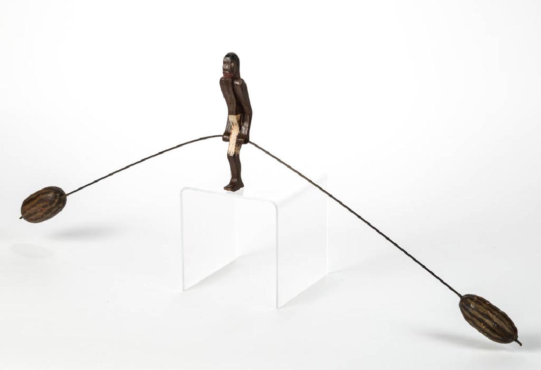 AMERICAN BLACK AMERICANA CARVED AND CUT-OUT WOOD: AMERICAN BLACK AMERICANA CARVED AND CUT-OUT WOOD BALANCE TOY, depicting a man in white shorts with a watermelon at each end of balance rod. Original painted surfaces. Circa 1920. Figure 6 1/4" H, 28 1