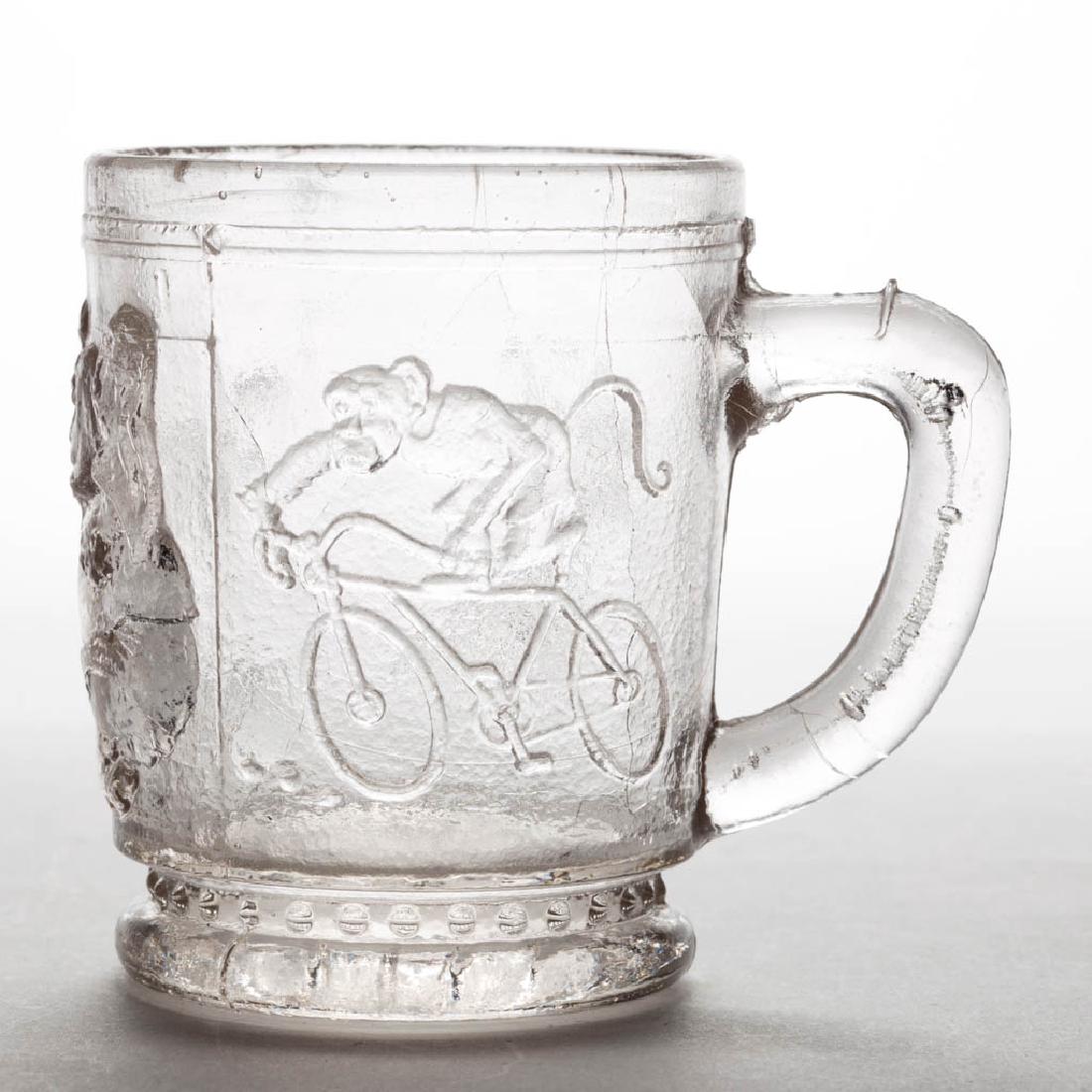 UNRECORDED CIRCUS ANIMALS CHILDREN'S MUG: UNRECORDED CIRCUS ANIMALS CHILDREN'S MUG, colorless, depicting a monkey riding a bicycle, an elephant chasing balls, and a wacko dog, beaded band above the foot, detail of beach ball under base. First