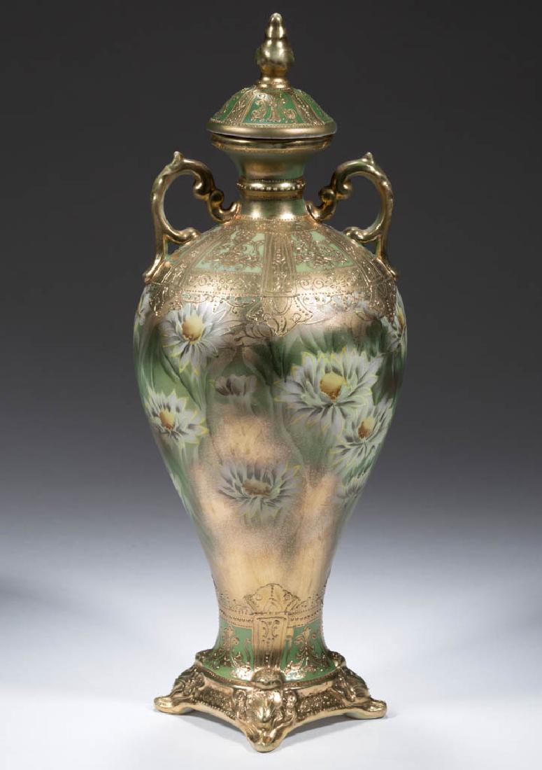NIPPON PORCELAIN COVERED URN: NIPPON PORCELAIN COVERED URN, baluster form with squared flared foot, ornate handles and small cover having molded finial; white aster floral design over green ground with gilding. Unmarked. First qua