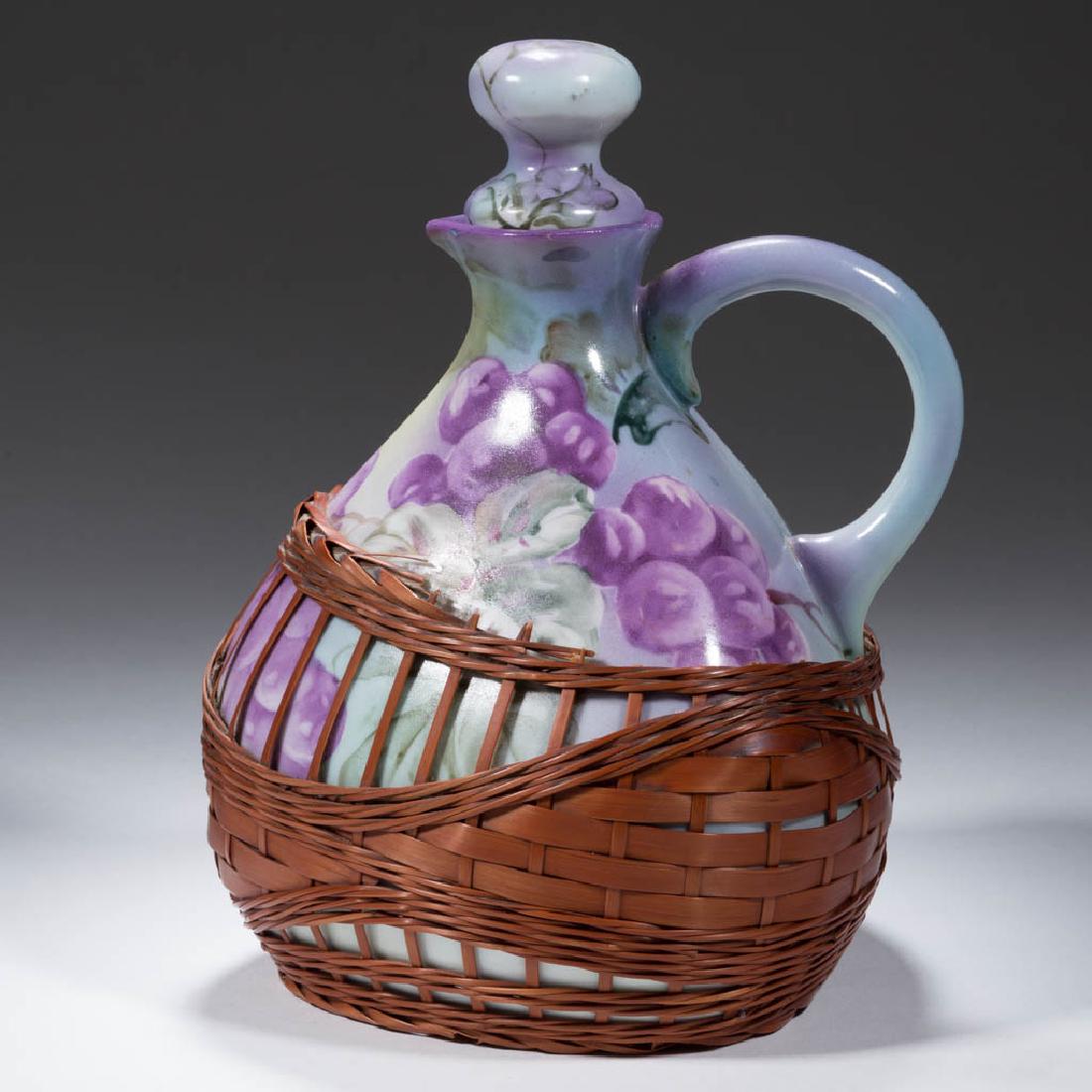 NIPPON PORCELAIN BASKETWEAVE EWER / WINE JUG: NIPPON PORCELAIN BASKETWEAVE EWER / WINE JUG, triangular squat form with one loop handle, hand-painted polychrome design of grapes and leaves on sides with brown woven material around shoulder and bas