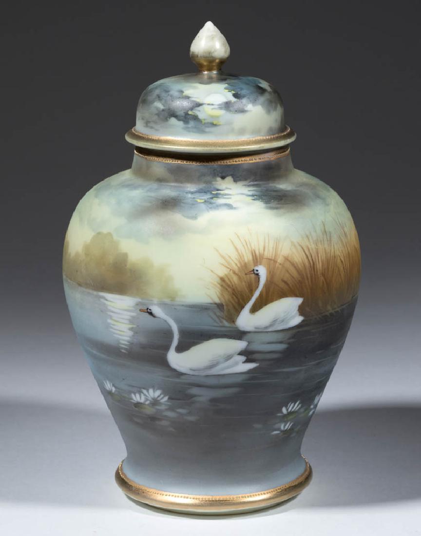 NIPPON PORCELAIN SWAN COVERED URN: NIPPON PORCELAIN SWAN COVERED URN, baluster form with raised cover, having hand-painted polychrome design of two swans with a lake landscape. Blue "Noritake / MADE IN JAPAN" with komaru symbol on base