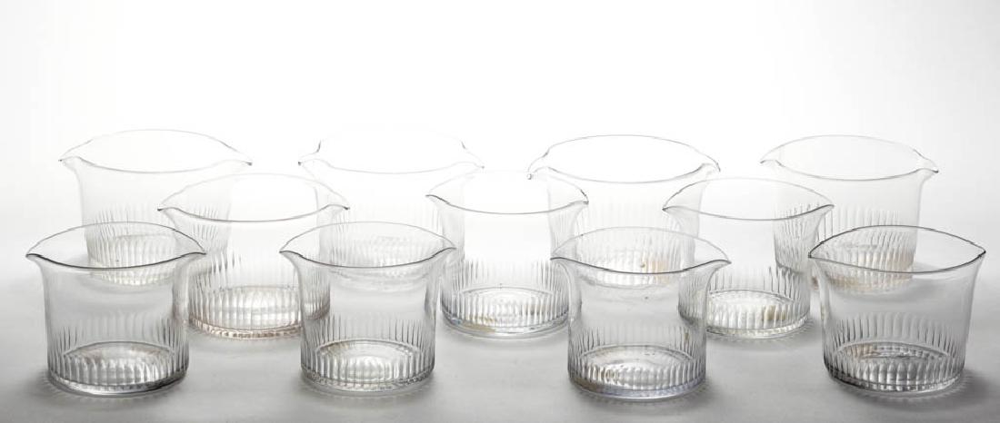 CUT FLUTE WINE RINSERS, ASSEMBLED SET OF 11: CUT FLUTE WINE RINSERS, ASSEMBLED SET OF 11, colorless, each of cylinder form with basal finger flutes, two spouts, and polished pontil marks. First half 19th century. 3 3/4" H, 4" and 4 1/2" D.Undama