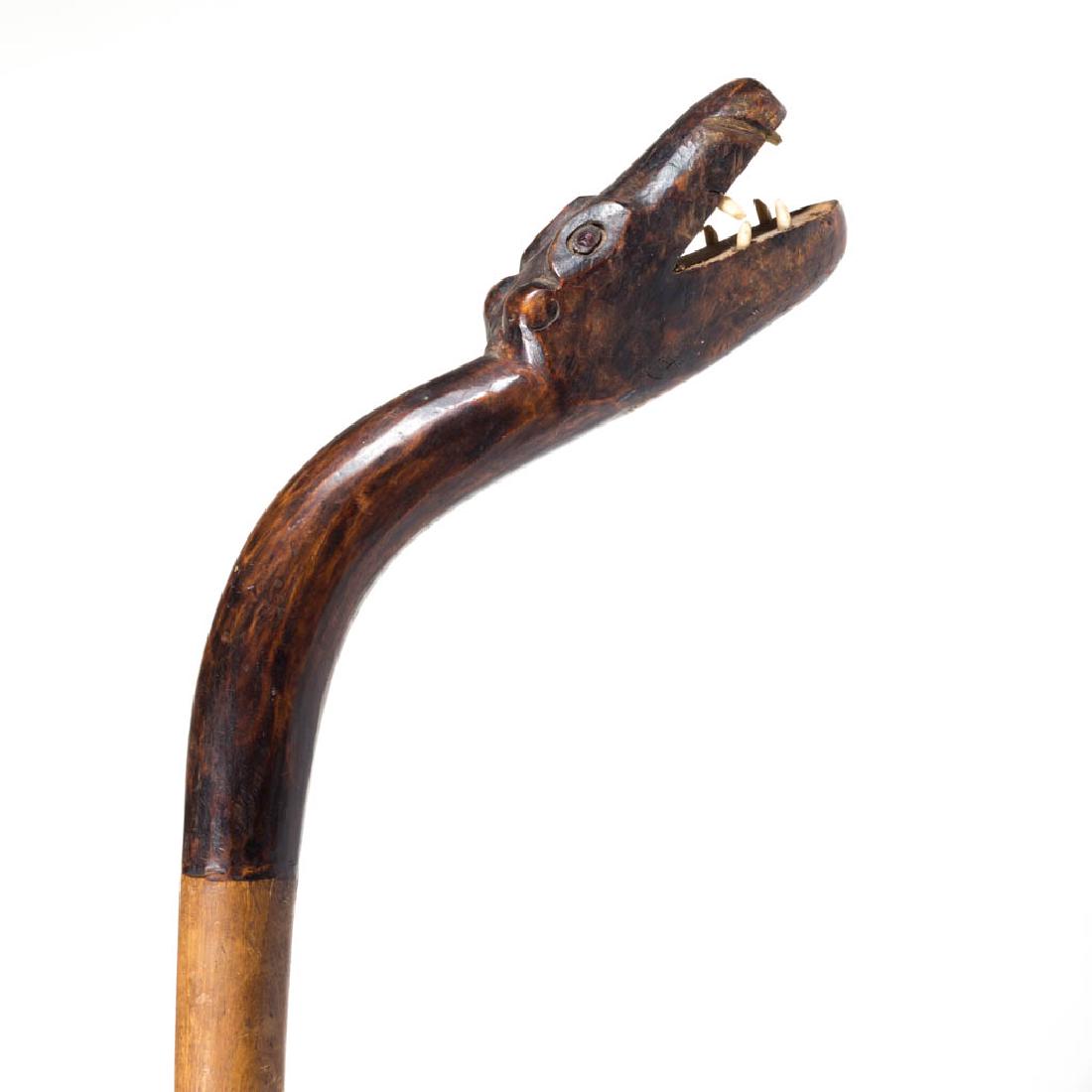 CARVED FOLK ART FIGURAL CANE / WALKING STICK: CARVED FOLK ART FIGURAL CANE / WALKING STICK, plain tapering cylindrical shaft with stylized bear-form handle, set with jeweled eyes and bone teeth. Old surface. First half 20th century. 41" L. Wear a