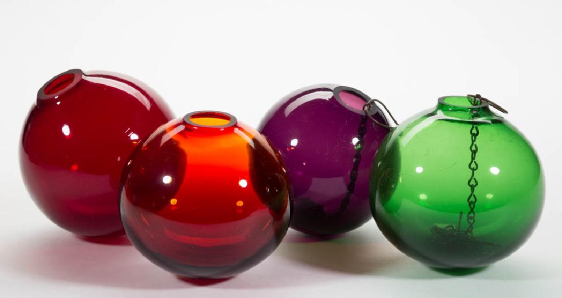 BLOWN GLASS WITCH BALLS, LOT OF FOUR: BLOWN GLASS WITCH BALLS, LOT OF FOUR, amethyst, green, and ruby, each with ground or polished openings, two with a chain and hook. Maker unverified. 20th century. 4" to 4 1/2" DOA. Undamaged with the 