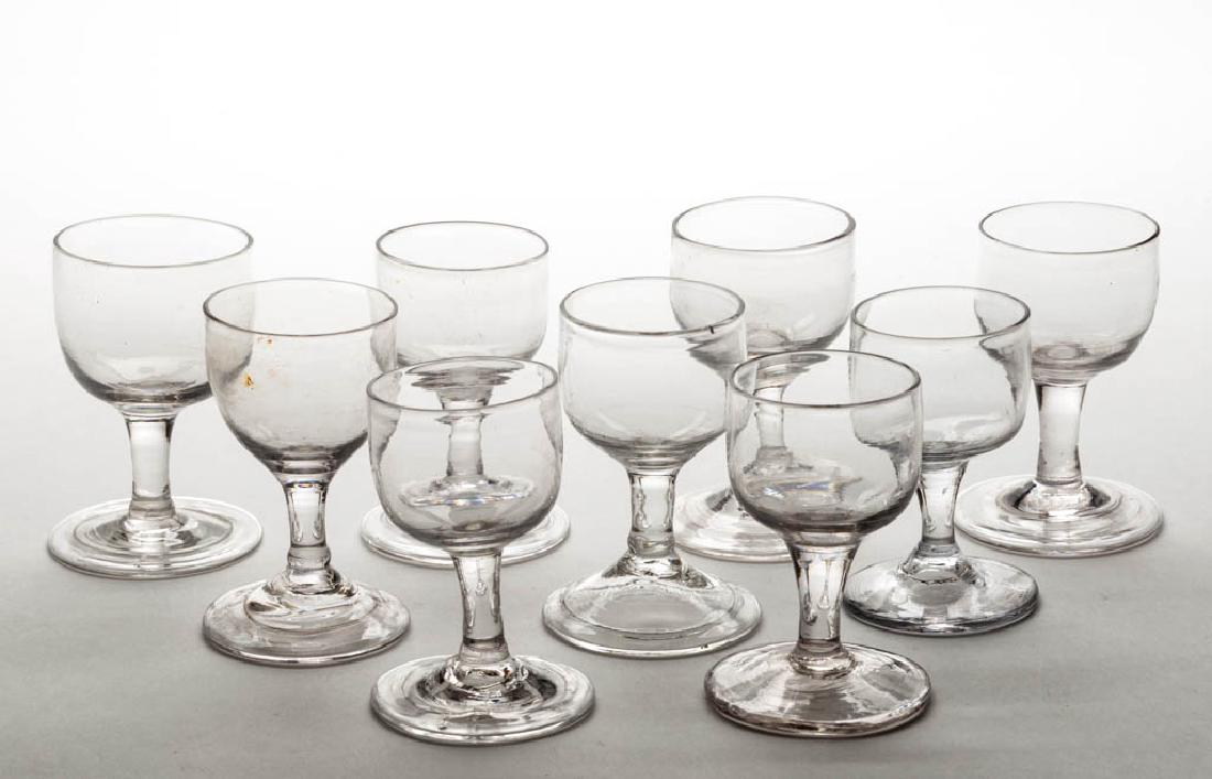 ASSORTED FREE-BLOWN WINE GLASSES, LOT OF NINE: ASSORTED FREE-BLOWN WINE GLASSES, LOT OF NINE, colorless lead glass, each ogee bowl raised on a drawn stem, seven with folded foot, each with rough pontil mark. First half 19th century. 3 1/4" to 3 1/