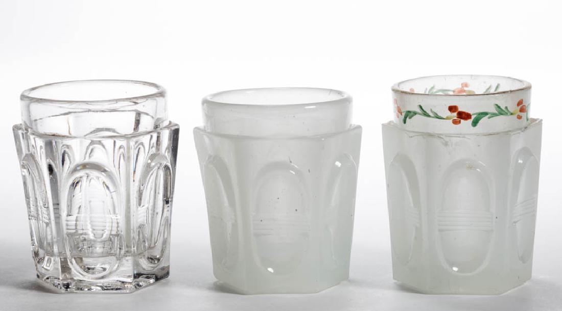 PRESSED BISECTED OVALS TOY TUMBLERS, LOT OF THREE: PRESSED BISECTED OVALS TOY TUMBLERS, LOT OF THREE, alabaster/clambroth and colorless, including one with paint decoration. 1850-1870. 2" H. Each with some chipping to the base. Provenance: From the es