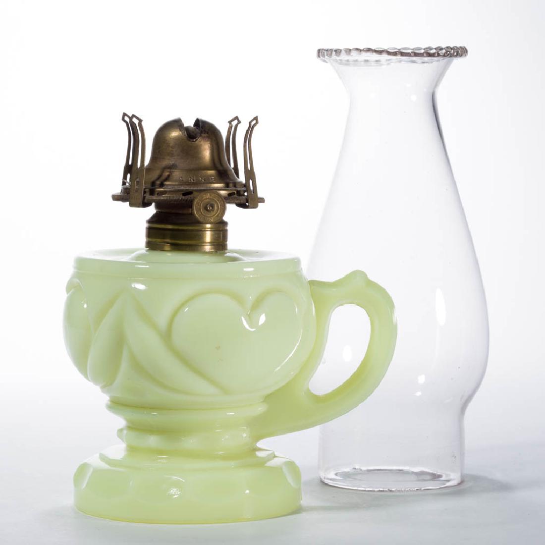 HEART KEROSENE FOOTED FINGER LAMP: HEART KEROSENE FOOTED FINGER LAMP, custard (reacts under black light), No. 1 Taplin-Brown collar. Fitted with a period No. 1"QUEEN ANNE" slip burner and colorless chimney with a beaded top. Tarentum G