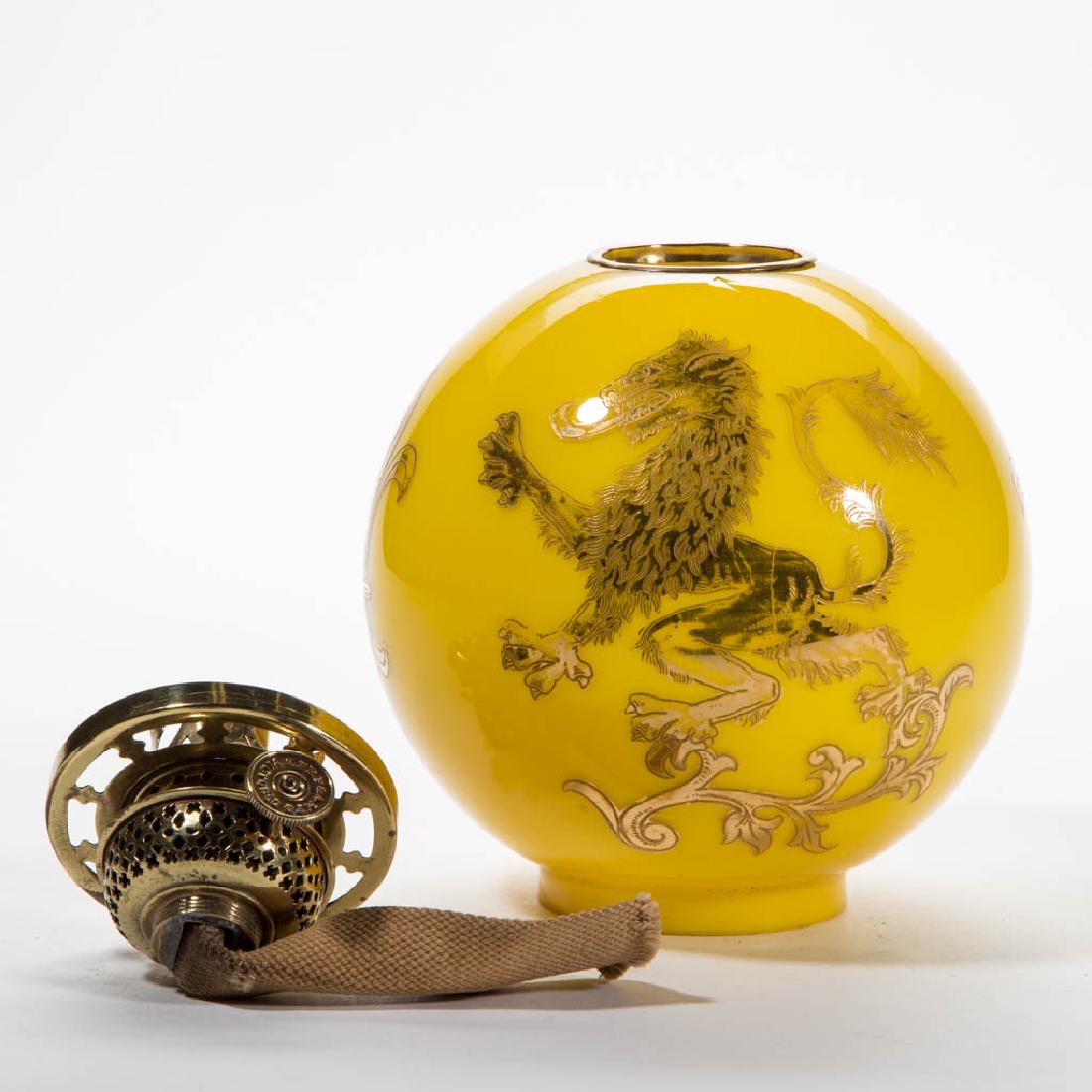 CASED GLASS DECORATED BALL-FORM SHADE: CASED GLASS DECORATED BALL-FORM SHADE, cased lemon yellow with lion rampant gold tracery, top with brass trim ring. Fitted with a period Plume & Atwood "VICTOR" slip burner and shade ring. Late 19th/e