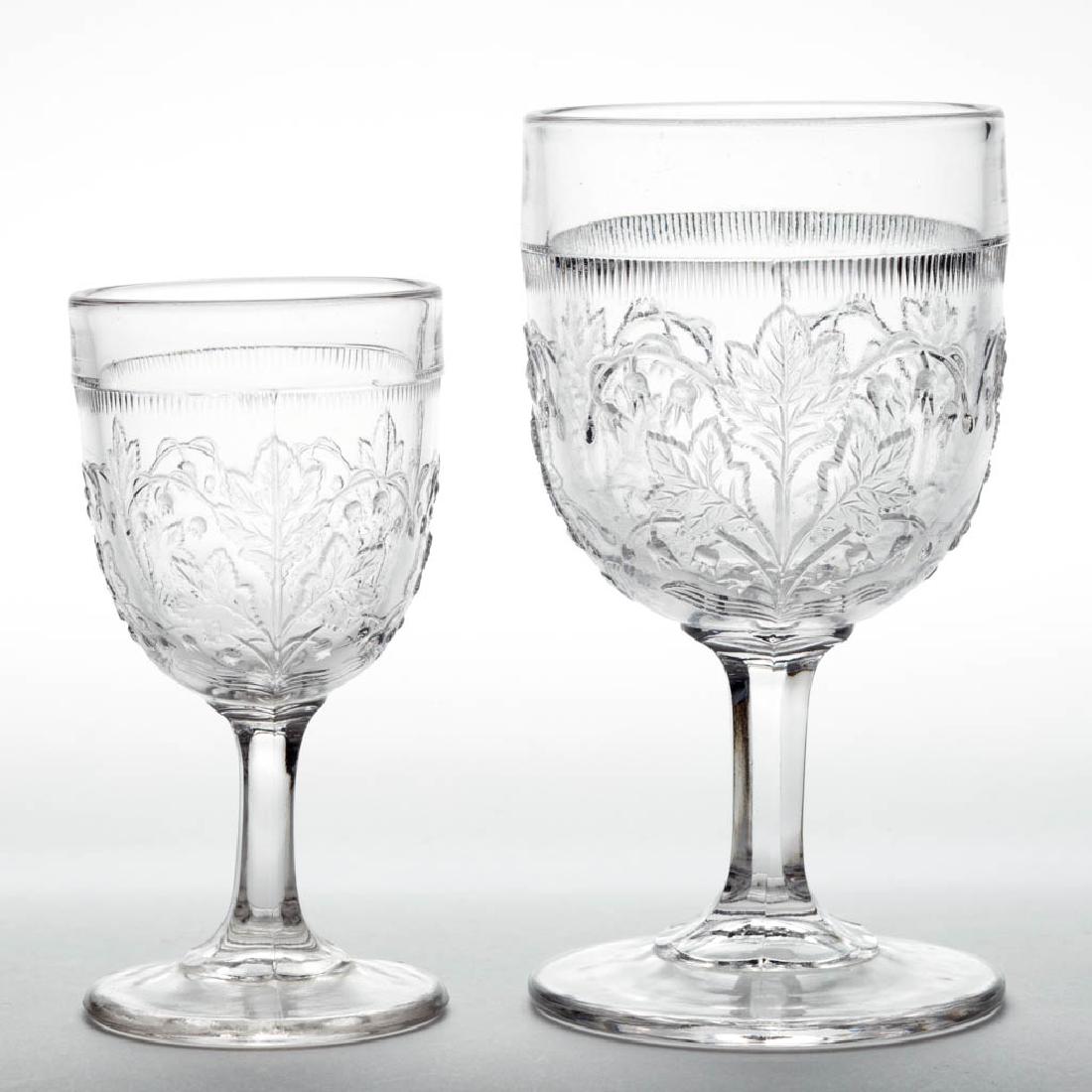 LILY OF THE VALLEY / MAY FLOWER (OMN) DRINKING: LILY OF THE VALLEY / MAY FLOWER (OMN) DRINKING ARTICLES, LOT OF TWO, colorless, comprising a champagne and a wine. Richards and Hartley Flint Glass Co. Fourth quarter 19th century. Champagne: 5" H, Wi