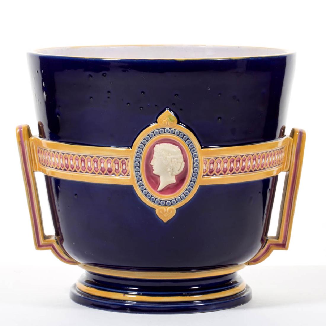 ENGLISH MINTON NEOCLASSICAL-STYLE MAJOLICA CERAMIC: ENGLISH MINTON NEOCLASSICAL-STYLE MAJOLICA CERAMIC JARDINIERE, polychrome decoration with cobalt ground, molded design to sides with two central cameos, two angular handles. Impressed "MINTON" and "11