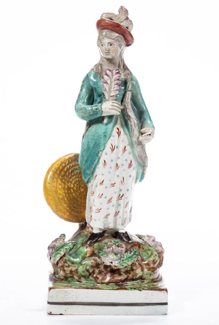 ENGLISH STAFFORDSHIRE PEARLWARE CERAMIC WOMAN ARCHERESS: ENGLISH STAFFORDSHIRE PEARLWARE CERAMIC WOMAN ARCHERESS FIGURE standing on a square and molded grassy base, with applied flower and leaf decoration, holding a bow in her left hand, a feathered arrow i