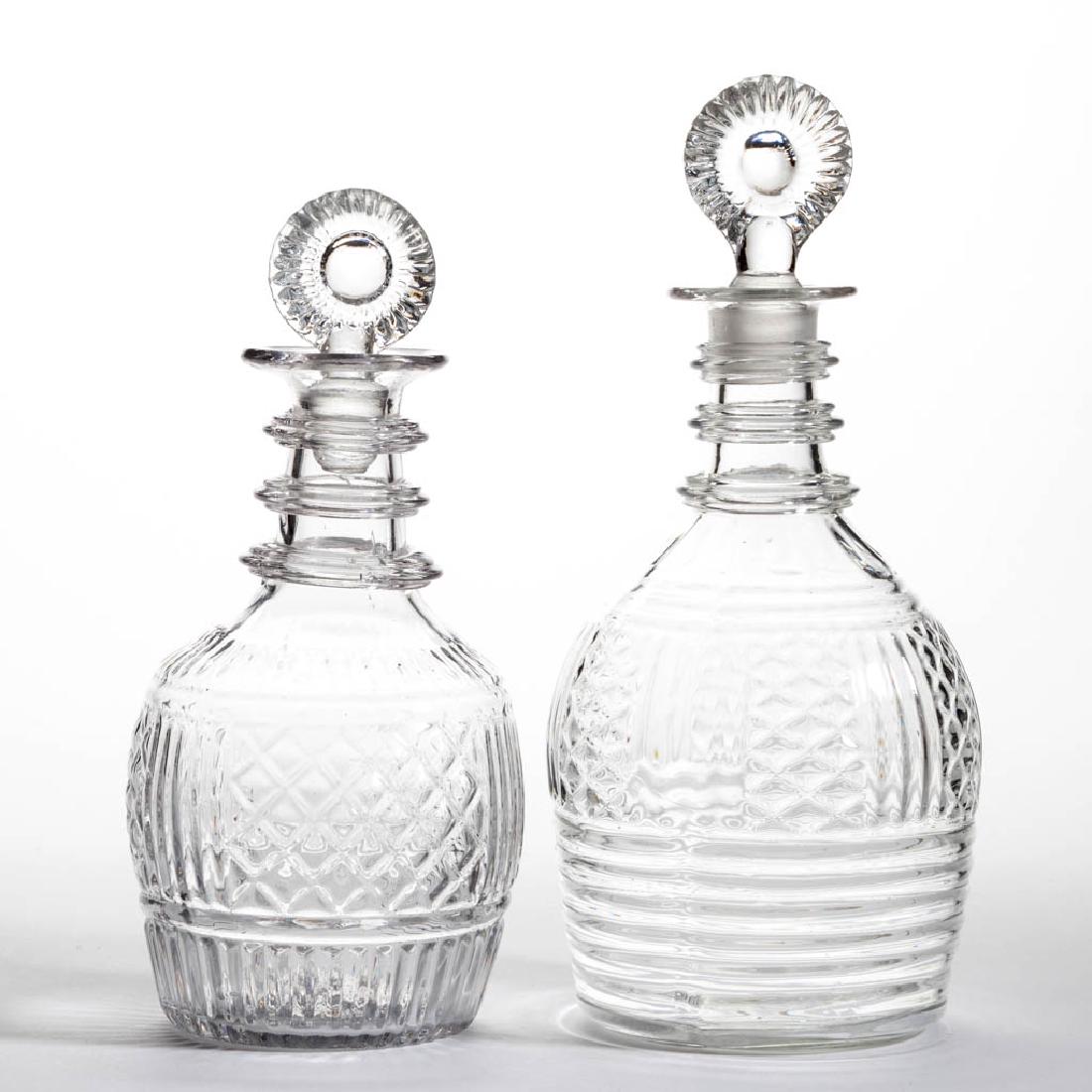 BLOWN-MOLDED THREE-MOLD DECANTERS, LOT OF TWO: BLOWN-MOLDED THREE-MOLD DECANTERS, LOT OF TWO, colorless, comprising a quart and pint example, each with panelled diamond motifs and pressed Type 21 stoppers. Probably English. First half 19th century
