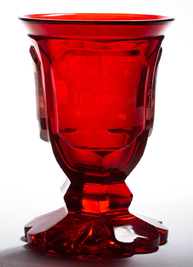 BOHEMIAN CUT AND ENGRAVED - RUBY-STAINED SPA BEAKER: BOHEMIAN CUT AND ENGRAVED - RUBY-STAINED SPA BEAKER, colorless, three-panel body with three reserves depicting Bohemian country scenes, panel-cut stem and foot with the base having a scalloped edge an