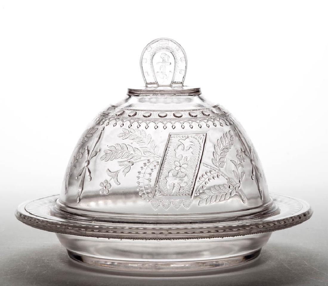 GOOD LUCK / HORSESHOE CHEESE DISH: GOOD LUCK / HORSESHOE CHEESE DISH, colorless, with Woman Churning Butter pattern in base. Fourth quarter 19th century. 6" HOA, 7 1/2" D. Nearly undamaged with some minor flaking to the base plateau an