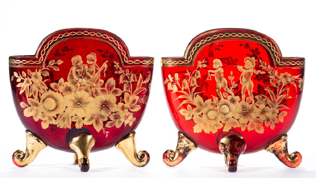 BOHEMIAN ENGRAVED AND GILT-DECORATED PILLOW VASES, LOT: BOHEMIAN ENGRAVED AND GILT-DECORATED PILLOW VASES, LOT OF TWO, ruby, long oblong-form with four applied feet, each depicting cherubs with instruments over a bed of floral decoration, reverse with flor