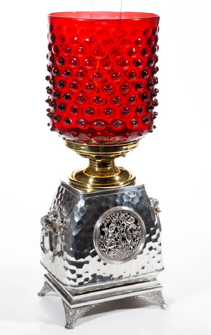 MERIDEN BRITANNIA SILVER-PLATED STAND LAMP: MERIDEN BRITANNIA SILVER-PLATED STAND LAMP, ruby cylinder-form hobnail shade, slightly tapered oblong-form font vase with overall honeycomb pattern, two circular windows with openwork cherubs in a gar