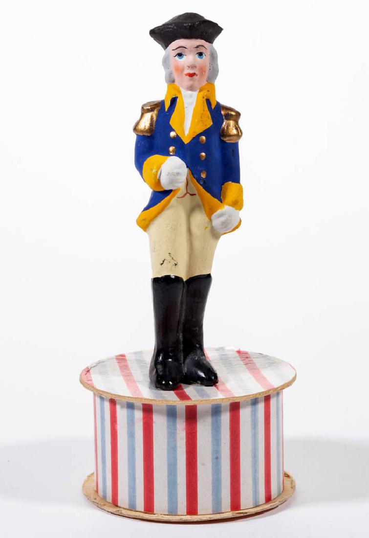 GERMAN COMPOSITION / PAPIER-MACHE SOLDIER CANDY: GERMAN COMPOSITION / PAPIER-MACHE SOLDIER CANDY CONTAINER, figure in uniform with tricorne hat, standing on a round cardboard box base, having polychrome-painted finish. Printed "Germany" partial mark
