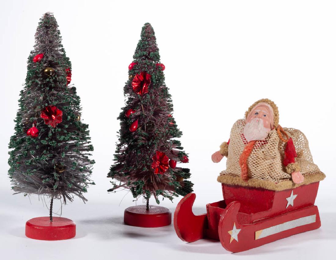 GERMAN SANTA CLAUS ON SLEIGH CANDY CONTAINER: GERMAN SANTA CLAUS ON SLEIGH CANDY CONTAINER, cardboard, celluloid, and fabric construction. Printed "GERMANY" mark to base. Together with two Christmas trees having foil and faux berry decoration. Th