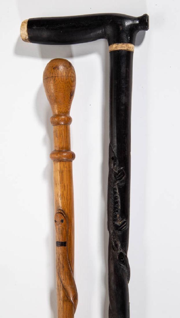 FOLK ART CARVED SNAKE CANES / WALKING STICKS, LOT OF: FOLK ART CARVED SNAKE CANES / WALKING STICKS, LOT OF TWO, each with serpent-entwined shaft, one possibly ebony with bone inserts, the other likely ash with knop handle and natural surface. Late 19th/e