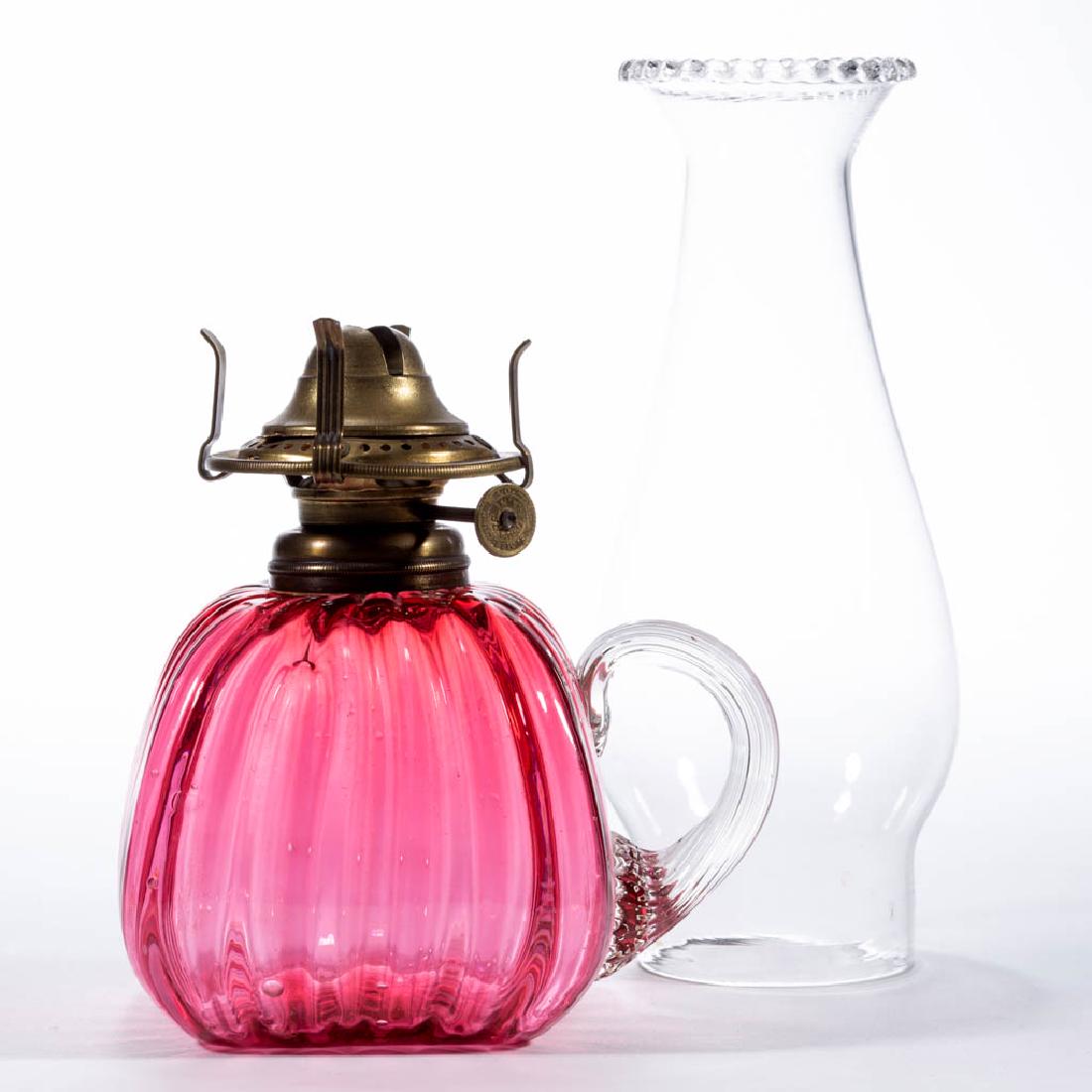 RIB-OPTIC KEROSENE FINGER LAMP: RIB-OPTIC KEROSENE FINGER LAMP, cased cranberry, slightly tapered square-form font, applied colorless reeded handle, period No. 1 collar. Fitted with a period No. 0 slip burner and colorless chimney. 