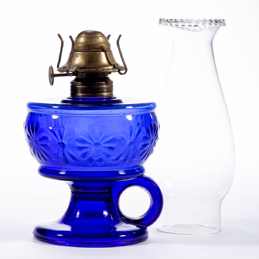 DAISY AND BOWKNOT KEROSENE FOOTED FINGER LAMP: DAISY AND BOWKNOT KEROSENE FOOTED FINGER LAMP, cobalt blue, No. 1 Taplin-Brown collar. Fitted with a period No. 2 slip burner and colorless chimney with beaded top. Cambridge Glass Co. Circa 1903. 9 1