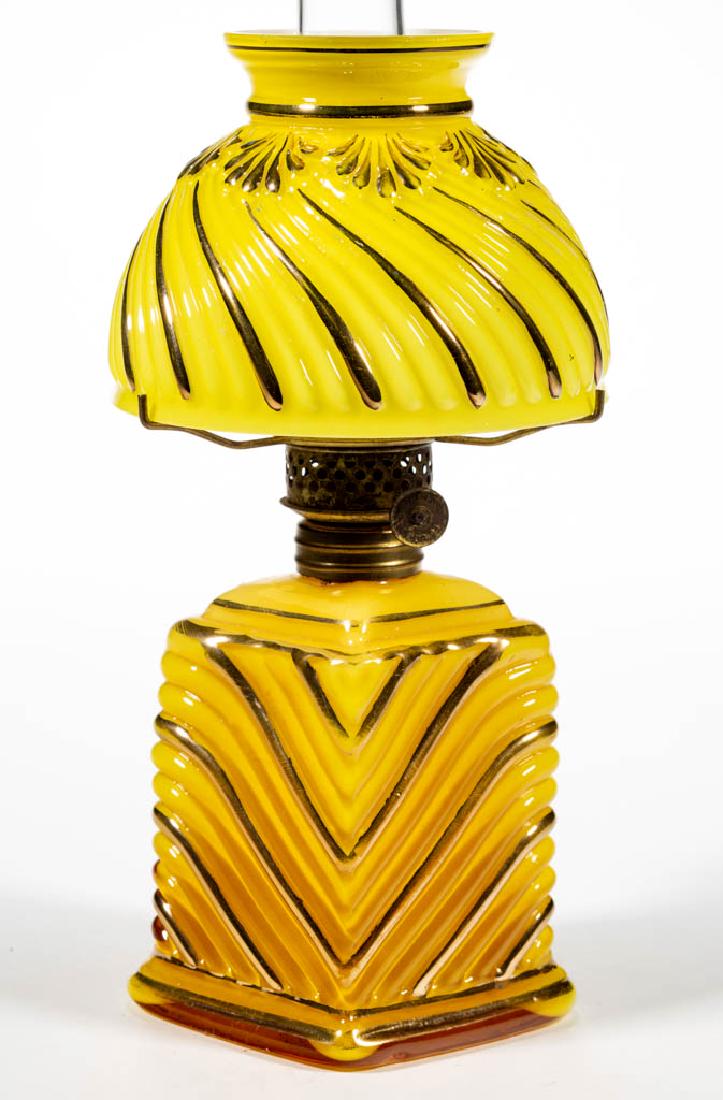RIB SWIRL CASED GLASS MINIATURE LAMP: RIB SWIRL CASED GLASS MINIATURE LAMP, cased mustard yellow with gilt decoration, diamond-form base with diagonal/Chevron-type ribs, lemon yellow umbrella shade with swirling ribs and leaf band to neck