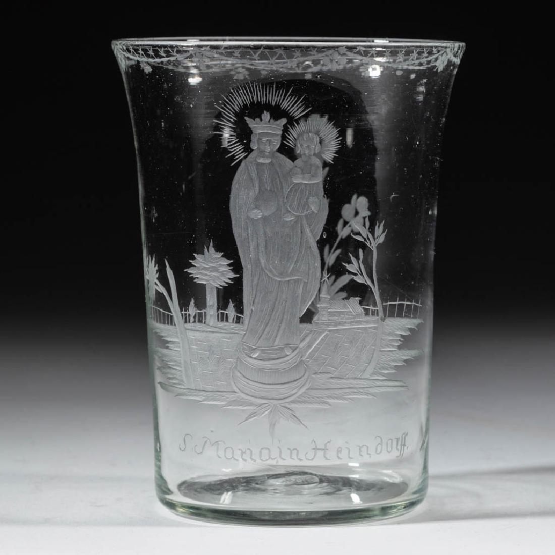 BOHEMIAN FREE-BLOWN AND ENGRAVED GLASS TUMBLER: BOHEMIAN FREE-BLOWN AND ENGRAVED GLASS TUMBLER, colorless, slightly tapered form featuring the Virgin Mary holding baby Jesus in a landscape with a church in the background, lettered "S. Manain Heindo