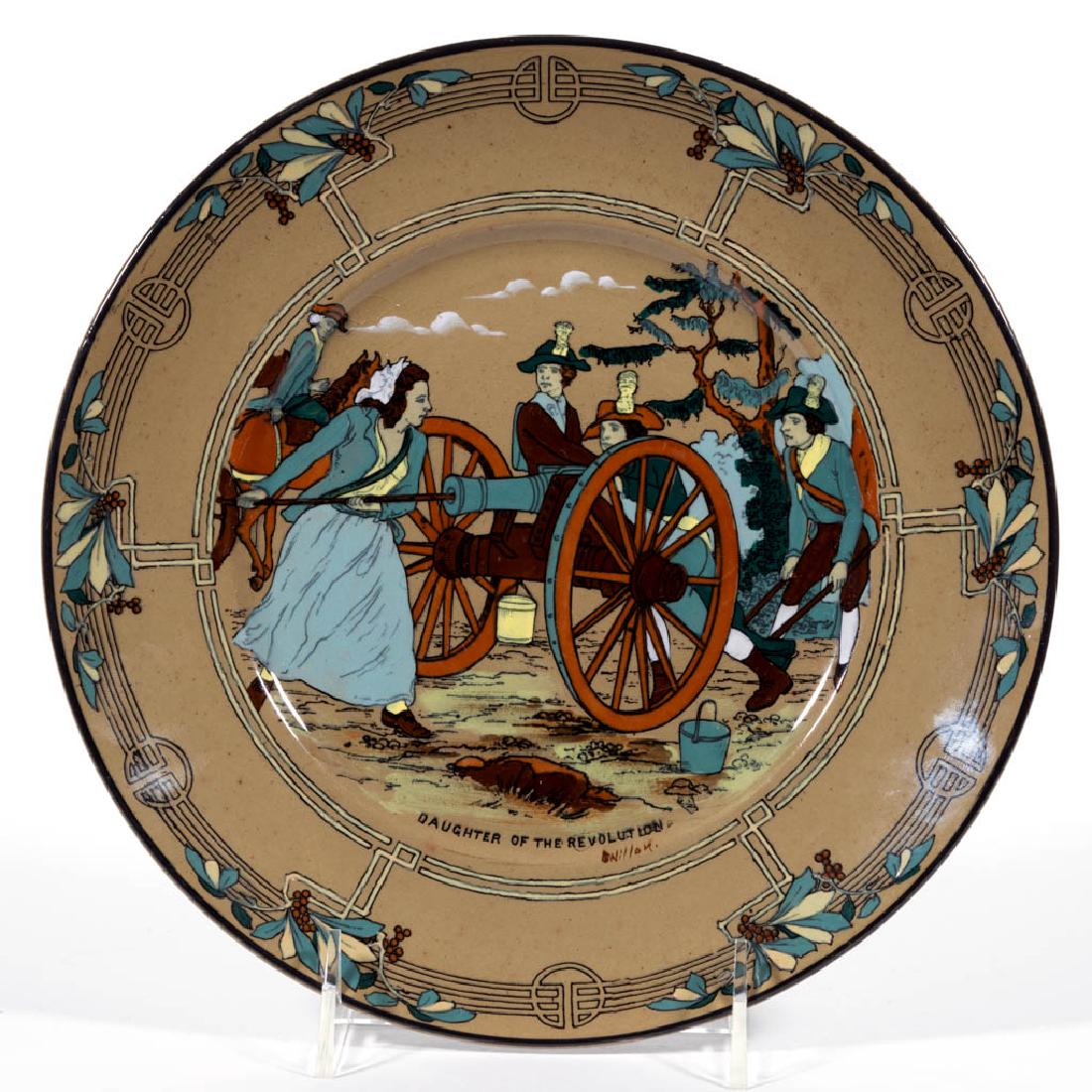 AMERICAN BUFFALO POTTERY DELDARE "DAUGHTER OF THE: AMERICAN BUFFALO POTTERY DELDARE "DAUGHTER OF THE REVOLUTION" CERAMIC PLATE, with image of a woman, probably Molly Pitcher, loading a cannon with soldiers waiting to fire, and signed "Nillon." Printed