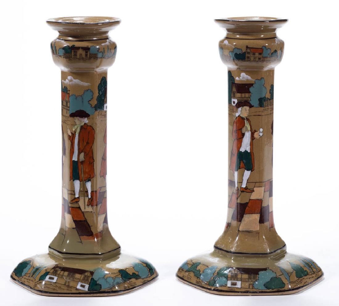 AMERICAN BUFFALO POTTERY DELDARE "YE OLDEN DAYS": AMERICAN BUFFALO POTTERY DELDARE "YE OLDEN DAYS" CERAMIC CANDLESTICK PAIR, with hand-painted scene of men in colonial dress conversing on sidewalk with period houses on top and bottom, signed. Printed