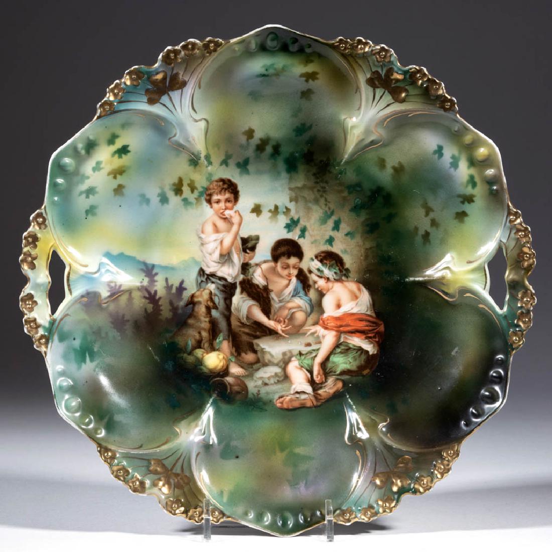 R.S. PRUSSIA PORCELAIN "DICE THROWERS" CAKE PLATE: R.S. PRUSSIA PORCELAIN "DICE THROWERS" CAKE PLATE, Mold 82, having open handles with central polychrome decal of Murillo's "Dice Throwers" depicting children playing games, with background shades of g