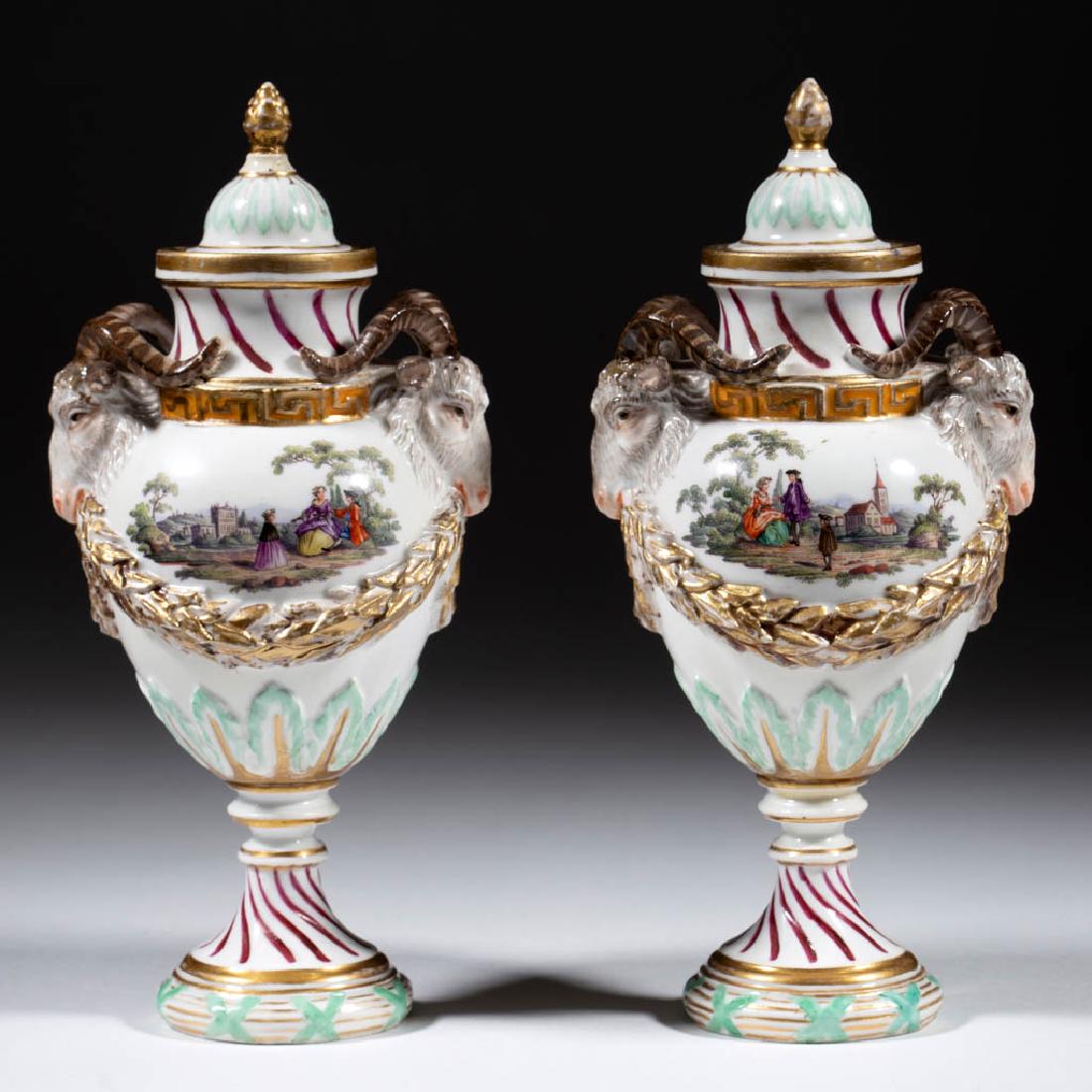 GERMAN DRESDEN PORCELAIN URNS, PAIR: GERMAN DRESDEN PORCELAIN URNS, PAIR, with rams head handles, hand-painted polychrome scenes with courting couples on each side, and molded gilt-decorated swag. Blue hand-brushed "AR" on underside. Dre