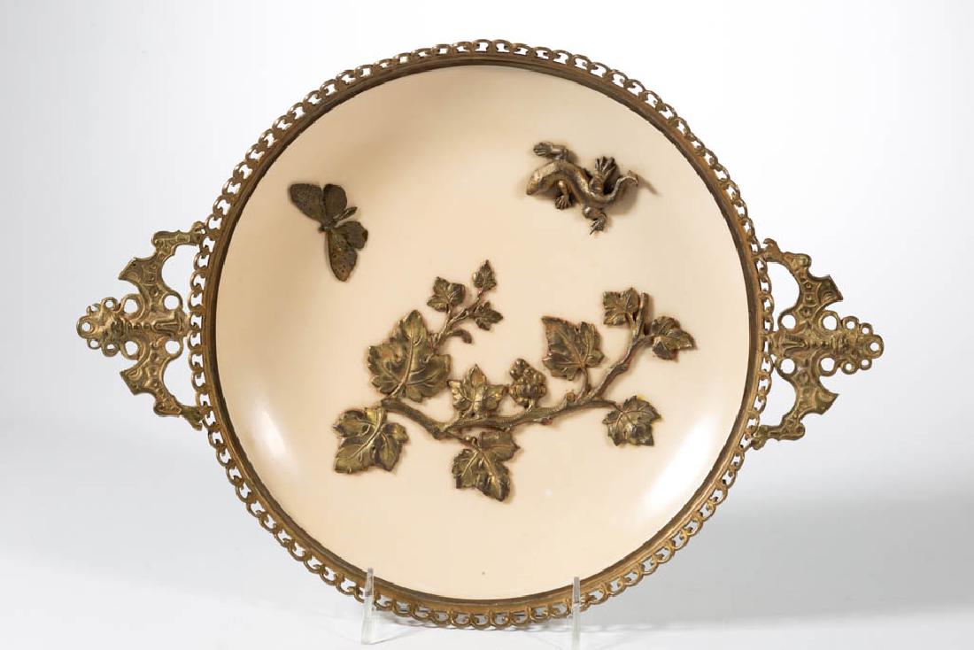 CONTINENTAL PORCELAIN ORMOLU-MOUNTED CHARGER: CONTINENTAL PORCELAIN ORMOLU-MOUNTED CHARGER, open-handled, having applied bronze lizard, butterfly, and grape vine decoration on cream ground. Unmarked. First half 20th century. 9 5/8" D sight, 10 1/