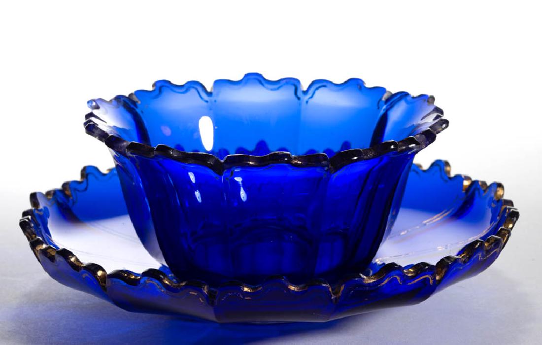 BOHEMIAN CUT GLASS FINGER BOWL AND UNDERPLATE: BOHEMIAN CUT GLASS FINGER BOWL AND UNDERPLATE, deep cobalt blue with gilt decoration, ten-panel bowl with a Moorish rim, 14-panel underplate with Moorish rim, each with a polished pontil mark. Second 