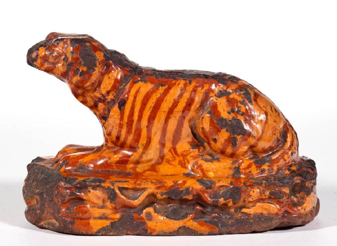 AMERICAN EARTHENWARE / REDWARE DOG / SPANIEL FIGURE: AMERICAN EARTHENWARE / REDWARE DOG / SPANIEL FIGURE, lead-glazed, solid recumbent form on an oblong base with tooled decoration to edge, combed slip decoration. First half 19th century. 3 1/2" H, 5 1/