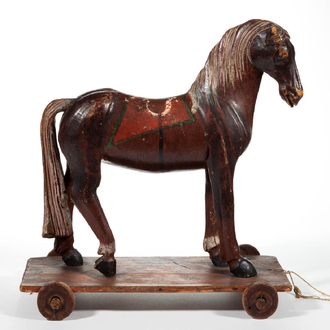 FOLK ART CARVED AND PAINTED HORSE PULL TOY: FOLK ART CARVED AND PAINTED HORSE PULL TOY, platform base with wooden wheels. Possibly original polychrome-painted surface. Fourth quarter 19th century. 14" HOA, 13" LOA, 7" WOA. Good overall visual c