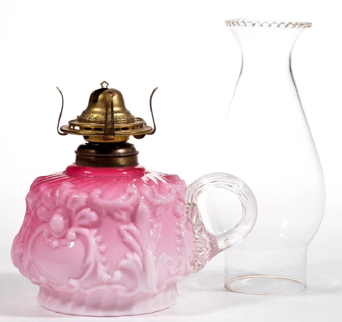 EMBOSSED CASED GLASS KEROSENE FINGER LAMP: EMBOSSED CASED GLASS KEROSENE FINGER LAMP, cased dark to light rose/pink, globular form, stylized pattern of acanthus leaves, beaded medallions and scrolling, colorless applied reeded handle, period N