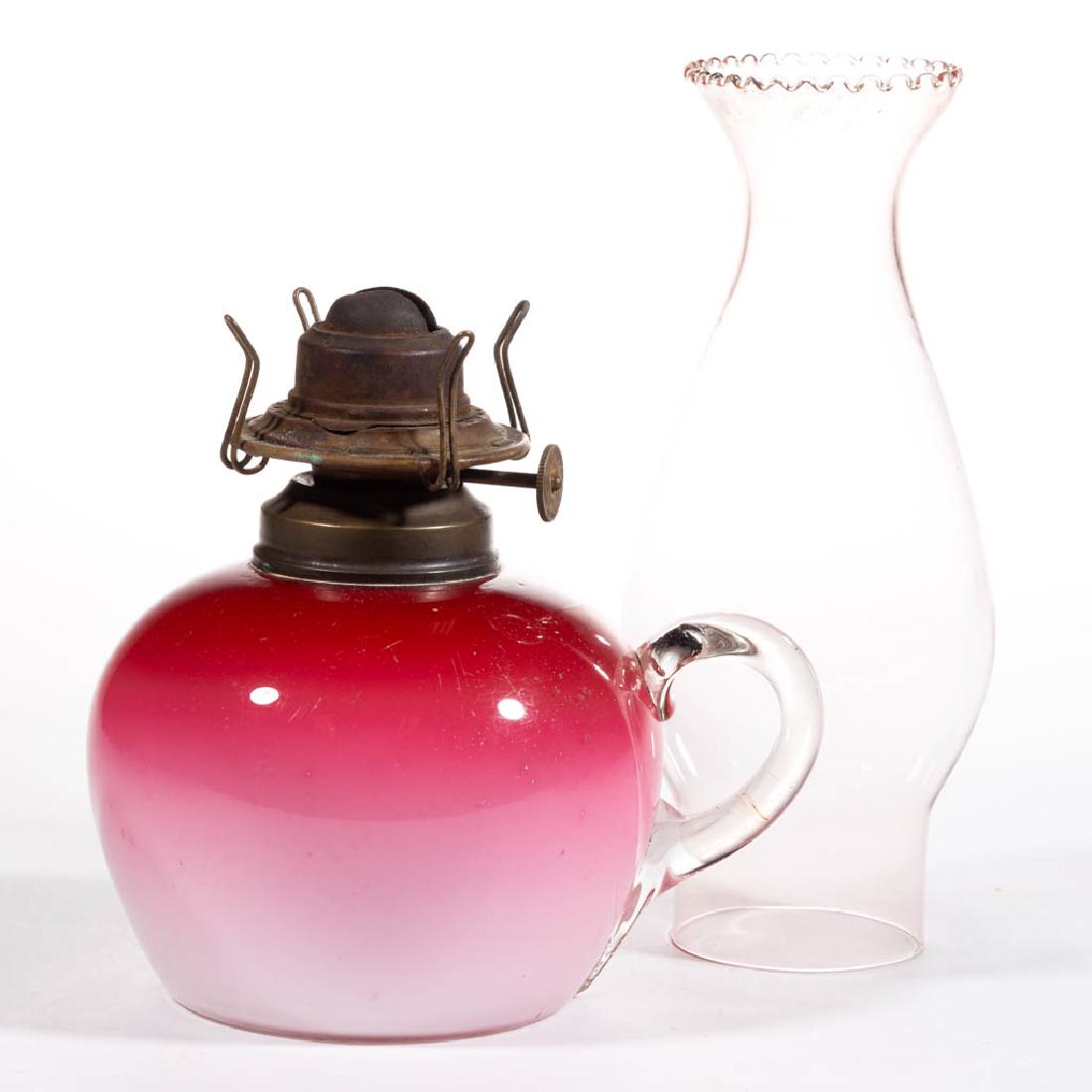 CASED GLASS KEROSENE FINGER LAMP: CASED GLASS KEROSENE FINGER LAMP, cased dark to light rose/pink, tapered form, colorless applied handle, period No. 1 collar. Fitted with a period setup comprising a No. 0 slip burner and colorless ch