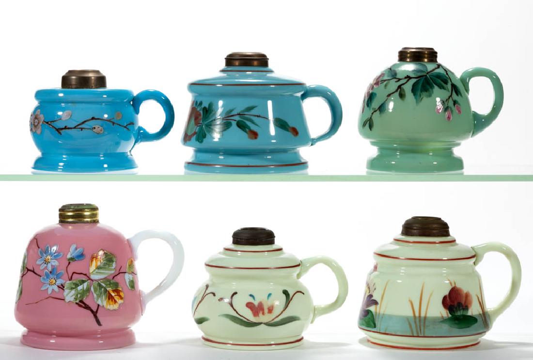 ASSORTED DECORATED OPAQUE GLASS KEROSENE FINGER LAMPS,: ASSORTED DECORATED OPAQUE GLASS KEROSENE FINGER LAMPS, LOT OF SIX, custard (reacts under black light), blue, jade green, and pink, each with polychrome floral decoration, various forms, applied handle