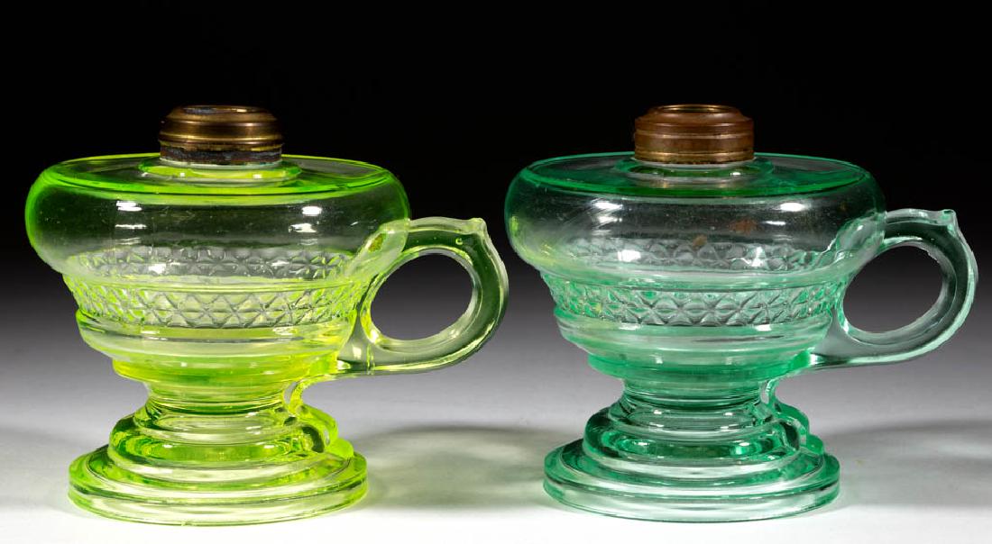 AQUARIUS KEROSENE FOOTED FINGER LAMPS, LOT OF TWO: AQUARIUS KEROSENE FOOTED FINGER LAMPS, LOT OF TWO, Vaseline and apple green (each reacts under black light), molded handles, each with a No. 1 brass collar. Fourth quarter 19th century. 4 1/4" H to to