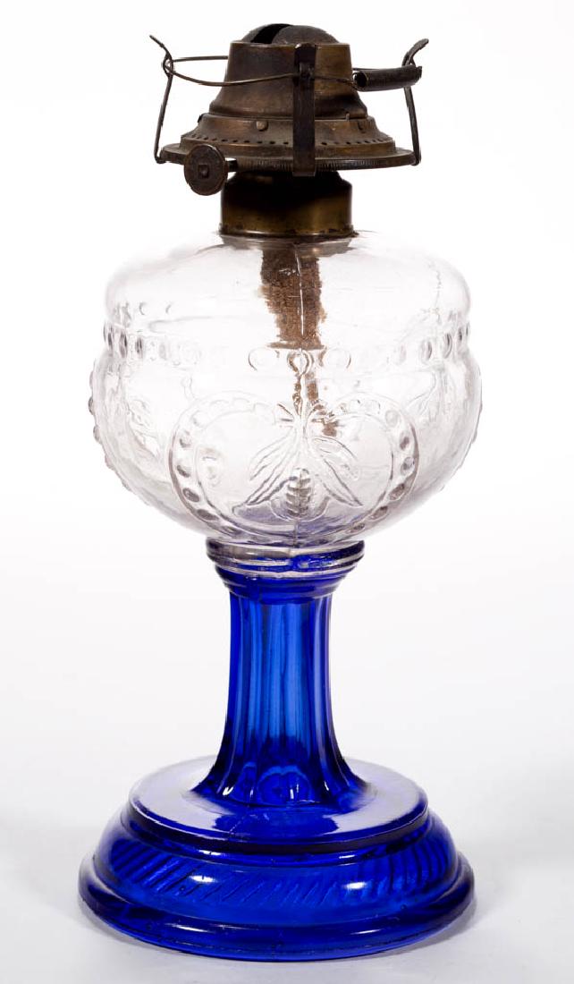 CORN IN SHIELD WITH CABLE BASE KEROSENE STAND LAMP: CORN IN SHIELD WITH CABLE BASE KEROSENE STAND LAMP, colorless font, cobalt blue base, period brass collar. Fitted with a period No. 1 slip burner with spring stabilizer. Central Glass Co. Fourth quart