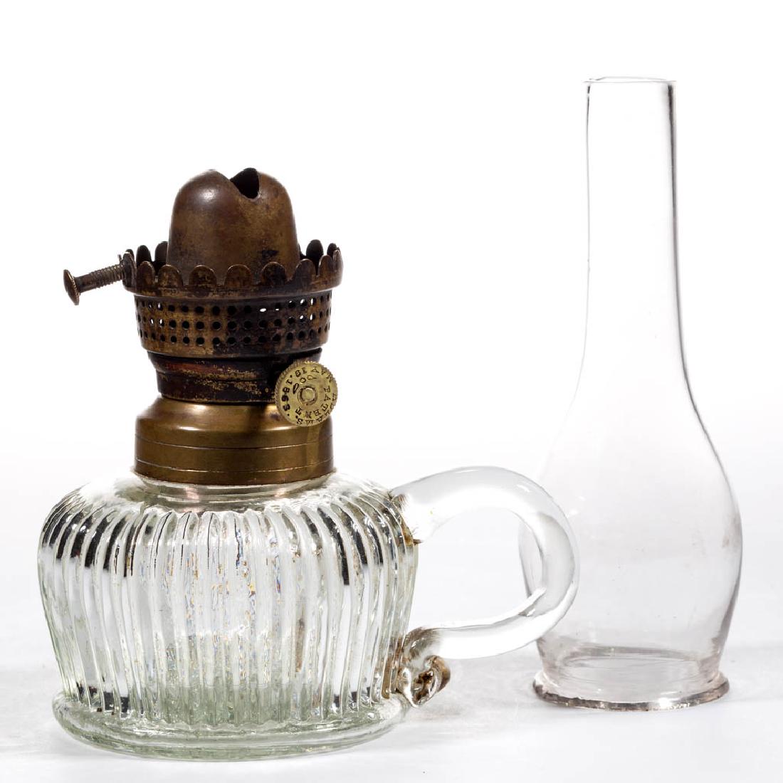 ADLAM'S NO. 0 KEROSENE LIP BURNER: ADLAM'S NO. 0 KEROSENE LIP BURNER, brass, thumbwheel marked "ADLAMS. PATENT MARCH 24. 1863" and with wing symbol, period colorless lip chimney. Fitted on a colorless Fine Rib finger lamp, colorless ap