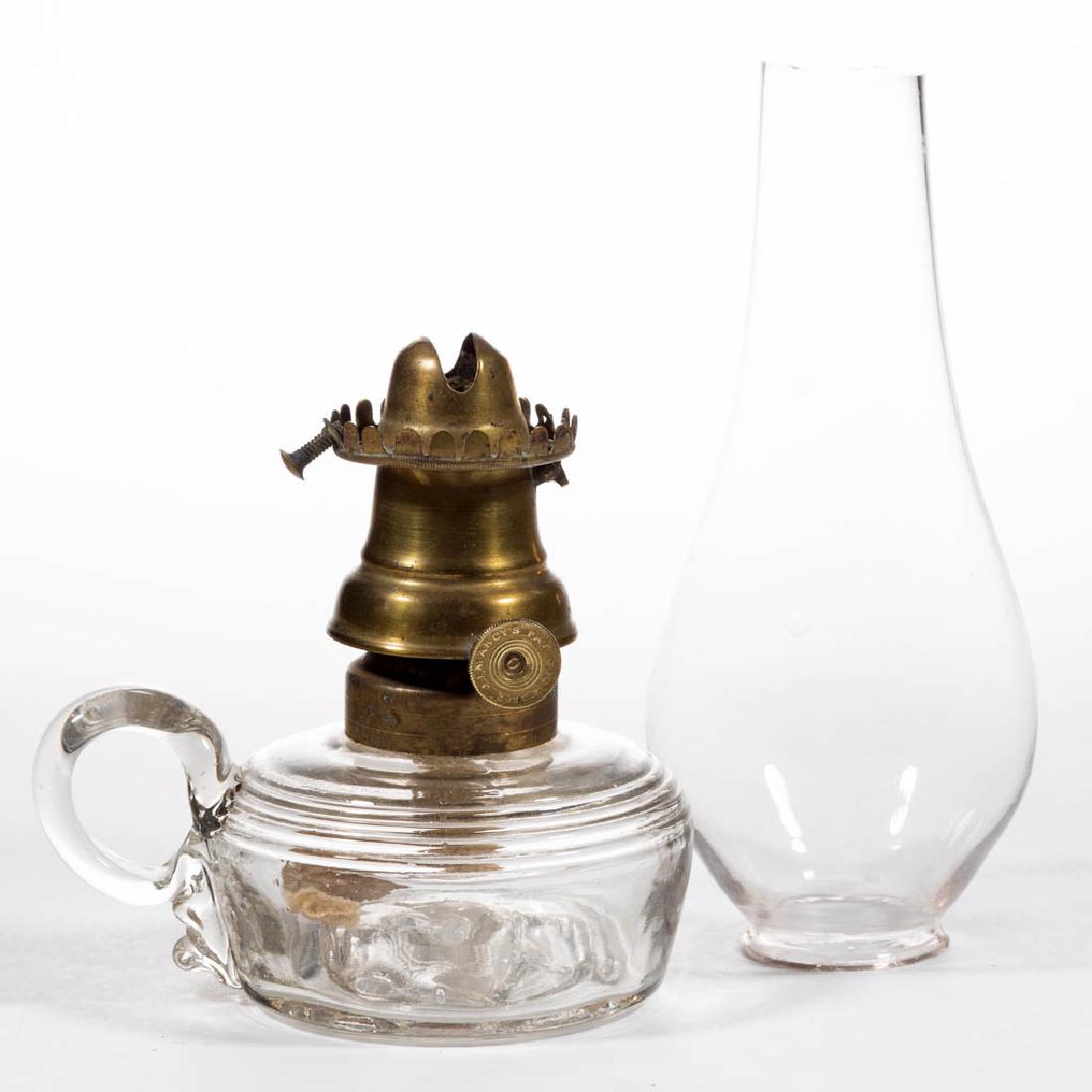 J. J. MARCY'S NO. 0 LIP BURNER: J. J. MARCY'S NO. 0 LIP BURNER, thumbwheel marked "JJ MARCY PAT. DEC: 2. 1862", colorless lip chimney. Fitted on a colorless finger lamp with horizontal bands and an eight-spoke cog to the base. Third