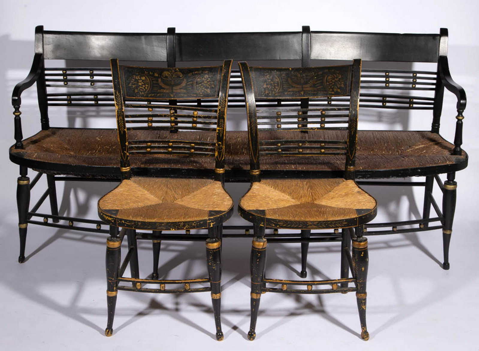 AMERICAN PAINT-DECORATED SEATING FURNITURE, LOT OF: AMERICAN PAINT-DECORATED SEATING FURNITURE, LOT OF THREE, settee and two side chairs, each with rush seat, ball-and-bar splat, and gold decoration against a black ground, chairs with stenciled crest r