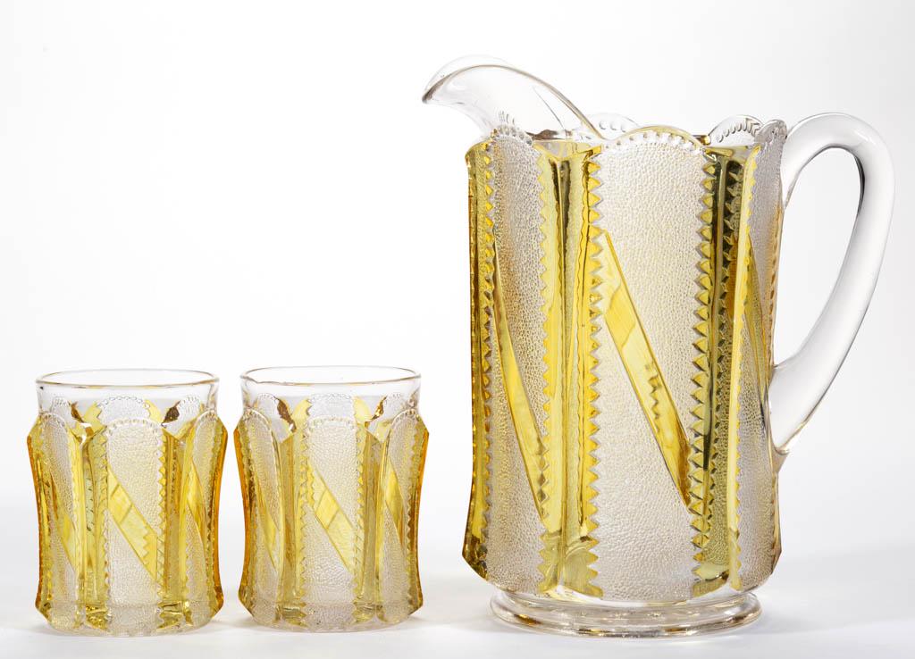 STIPPLED BAR - AMBER-STAINED THREE-PIECE WATER SET: STIPPLED BAR - AMBER-STAINED THREE-PIECE WATER SET, colorless, comprising a water pitcher and two tumblers. U. S. Glass Co. Pattern introduced in 1895. Pitcher: 8 5/8" H. Tumblers: 3 7/8" H.Pitcher in